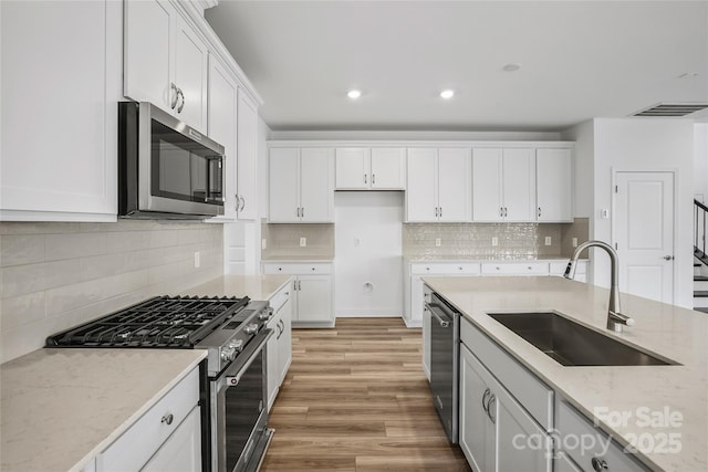 kitchen with a sink, visible vents, white cabinetry, appliances with stainless steel finishes, and light stone countertops