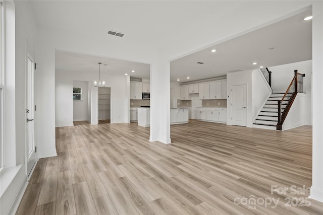 unfurnished living room featuring light wood finished floors, visible vents, stairs, a notable chandelier, and recessed lighting