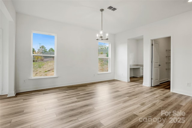 unfurnished dining area with baseboards, visible vents, light wood finished floors, and an inviting chandelier