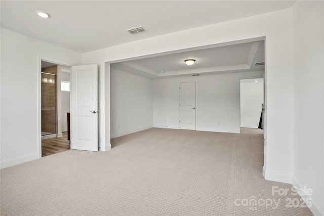 unfurnished bedroom with baseboards, visible vents, a raised ceiling, and light colored carpet