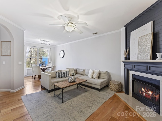 living area featuring arched walkways, a fireplace, visible vents, ornamental molding, and light wood finished floors