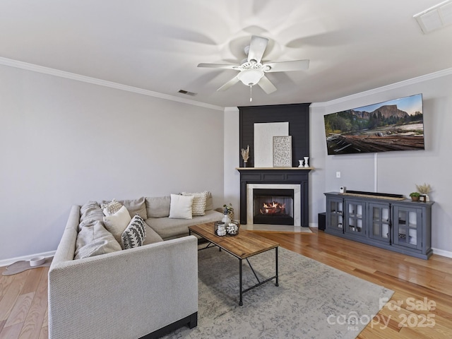 living area with a fireplace with flush hearth, wood finished floors, visible vents, and crown molding