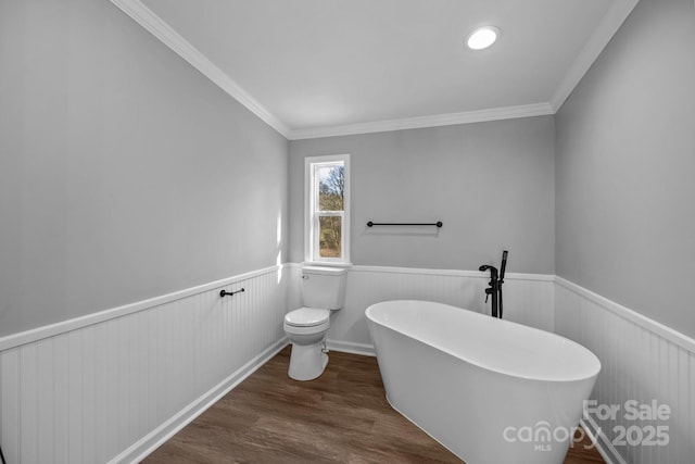 bathroom with a wainscoted wall, a soaking tub, wood finished floors, and toilet