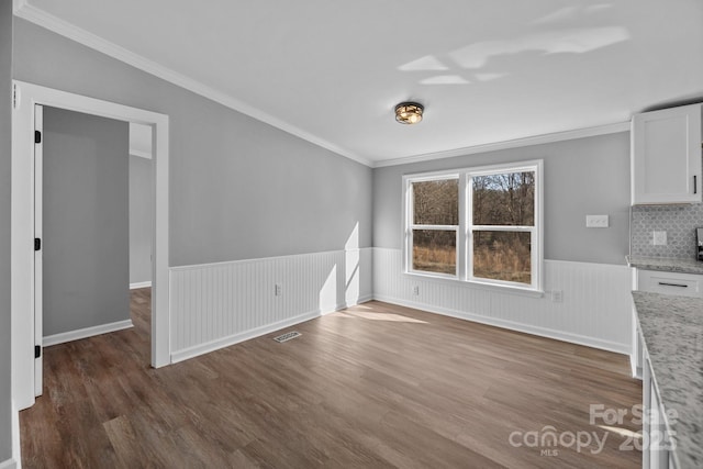 unfurnished dining area with a wainscoted wall, wood finished floors, visible vents, and crown molding