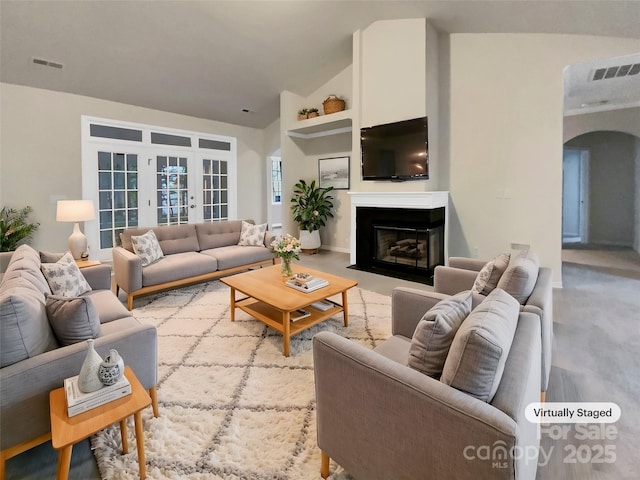 living area with arched walkways, french doors, visible vents, a fireplace with flush hearth, and vaulted ceiling