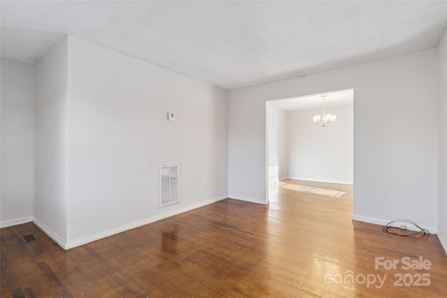 spare room featuring an inviting chandelier, baseboards, visible vents, and wood finished floors