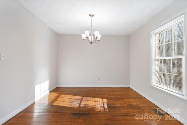 empty room with dark wood-style floors, baseboards, visible vents, and a chandelier