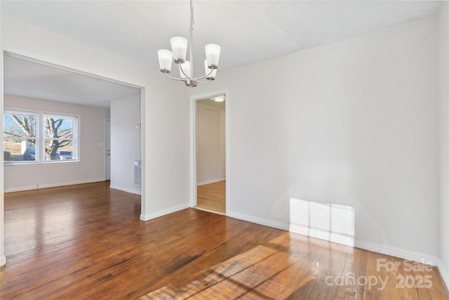 empty room with dark wood-type flooring, a chandelier, and baseboards