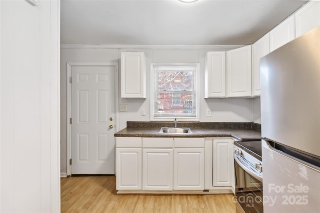 kitchen featuring electric stove, dark countertops, freestanding refrigerator, white cabinetry, and a sink