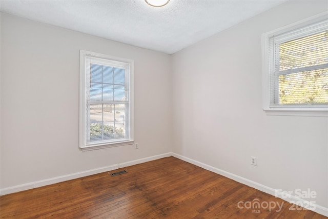 empty room with a healthy amount of sunlight, visible vents, baseboards, and wood finished floors