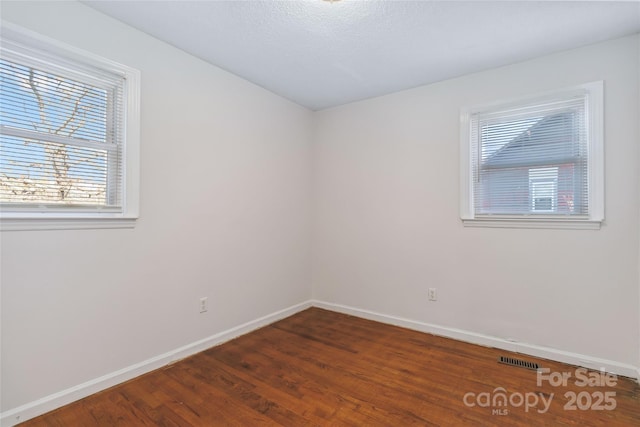 empty room with visible vents, baseboards, and dark wood-type flooring