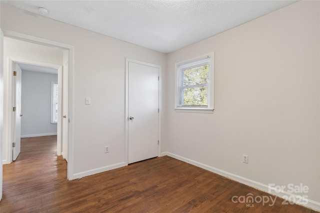 unfurnished bedroom with a textured ceiling, dark wood-type flooring, and baseboards