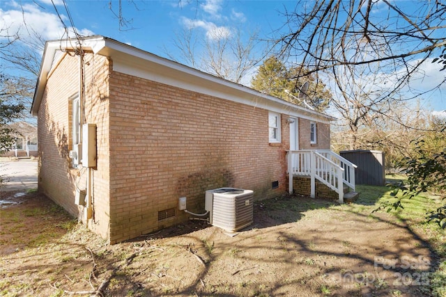 view of side of property featuring an outbuilding, brick siding, a storage unit, central AC unit, and crawl space