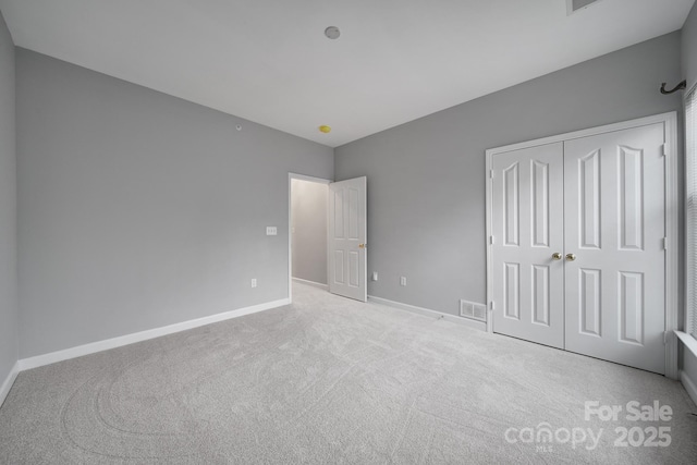 unfurnished bedroom featuring light carpet, a closet, visible vents, and baseboards