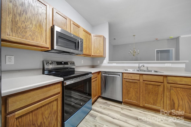 kitchen with light wood finished floors, appliances with stainless steel finishes, decorative light fixtures, light countertops, and a sink