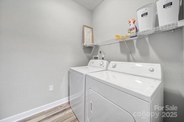 clothes washing area with laundry area, baseboards, washer and clothes dryer, and light wood finished floors