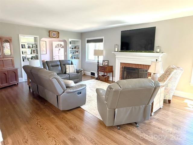 living area featuring a brick fireplace, light wood-style flooring, visible vents, and baseboards