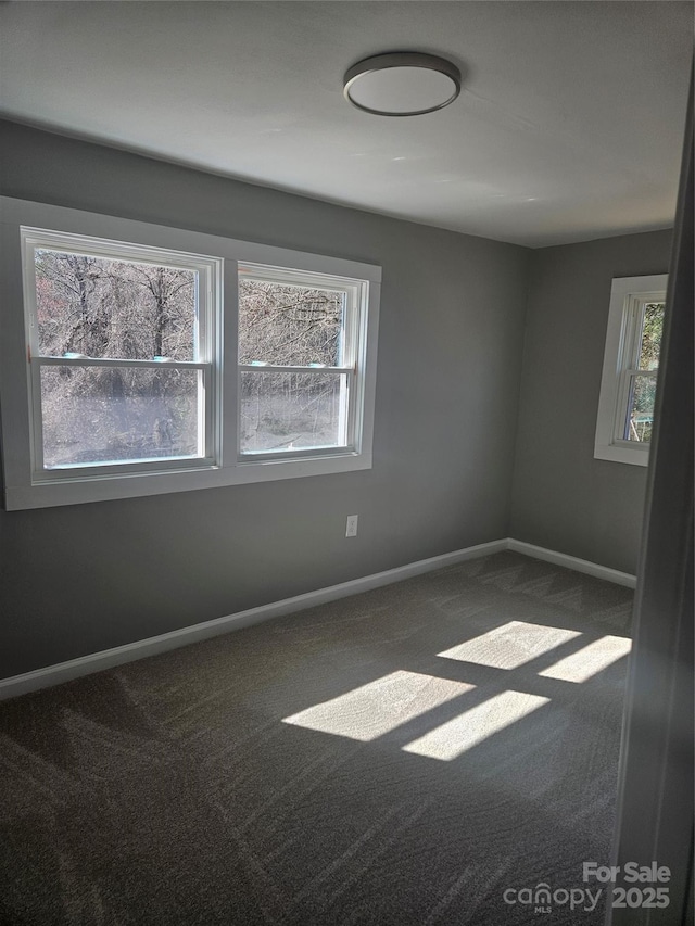 spare room with plenty of natural light, dark carpet, and baseboards