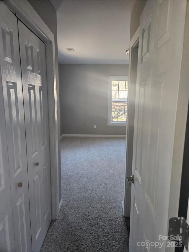 hallway with carpet, visible vents, and baseboards