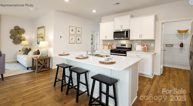 kitchen with an island with sink, stainless steel appliances, a sink, and light countertops