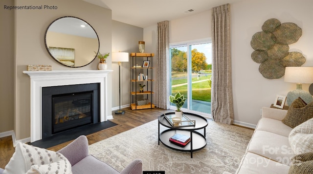 living area featuring a fireplace with flush hearth, visible vents, baseboards, and wood finished floors