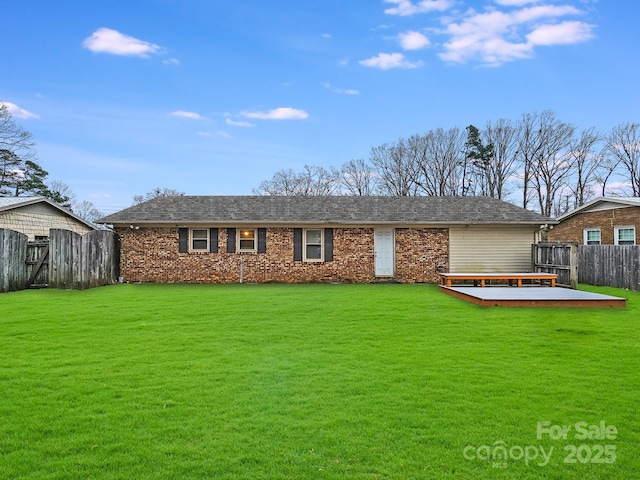 view of front facade with a deck, brick siding, a front yard, and fence