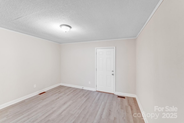 spare room featuring a textured ceiling, ornamental molding, light wood-style flooring, and baseboards