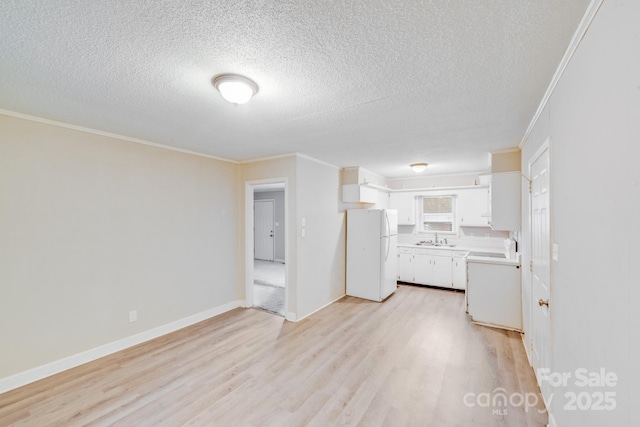 kitchen with white cabinets, freestanding refrigerator, light countertops, light wood-type flooring, and a sink