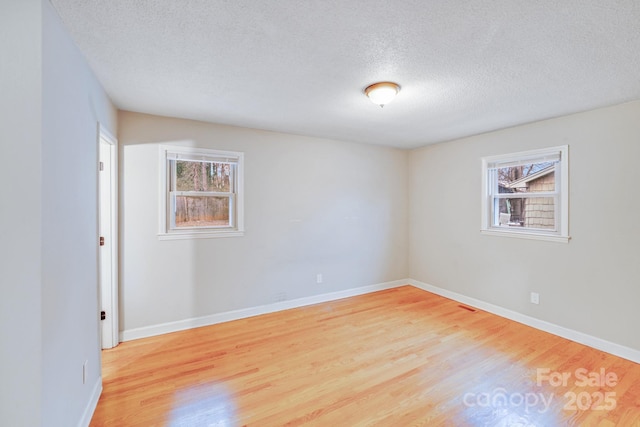 empty room with baseboards, a textured ceiling, and light wood finished floors