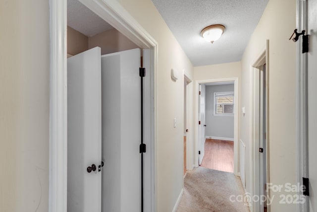 hall with a textured ceiling, light carpet, and baseboards