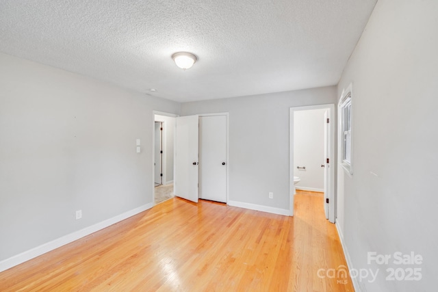 unfurnished bedroom featuring a textured ceiling, baseboards, wood finished floors, and ensuite bathroom