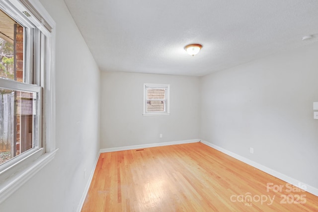 empty room with plenty of natural light, wood finished floors, and baseboards