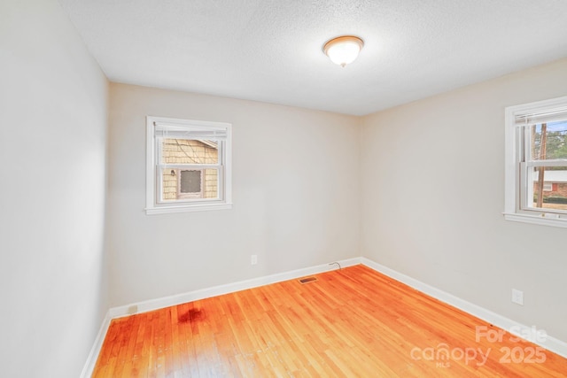 unfurnished room with a textured ceiling, wood finished floors, and baseboards