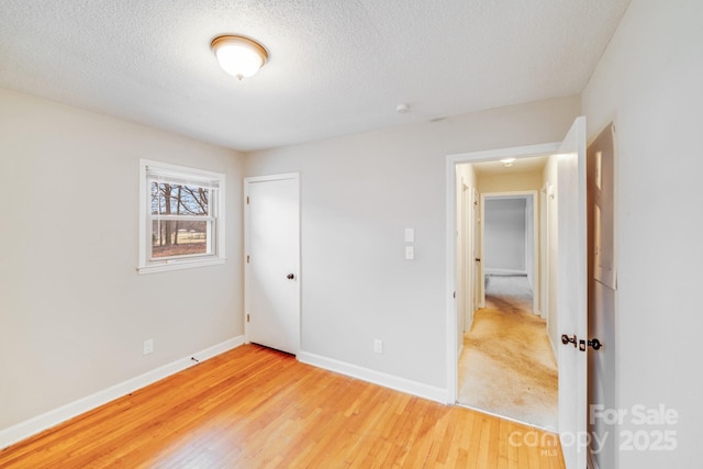 unfurnished bedroom featuring baseboards, a textured ceiling, a closet, and light wood-style floors