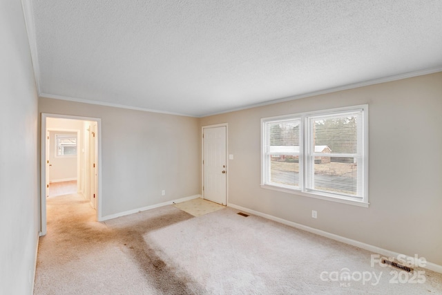 unfurnished room featuring ornamental molding, light carpet, a textured ceiling, and baseboards