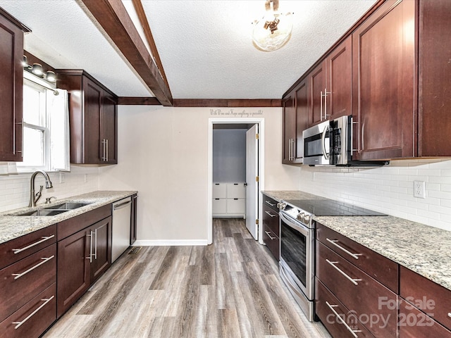 kitchen with a sink, baseboards, appliances with stainless steel finishes, light stone countertops, and light wood finished floors