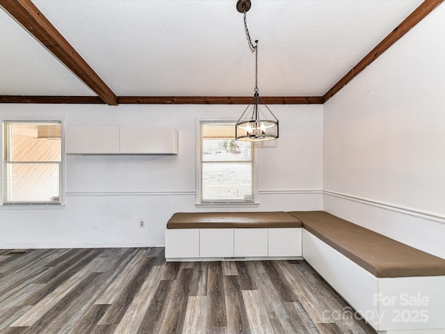 unfurnished dining area featuring dark wood-style flooring, a notable chandelier, a textured ceiling, and beam ceiling