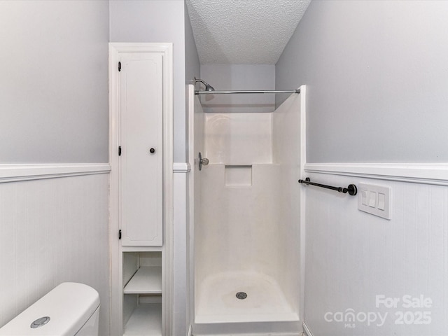 bathroom with a shower stall, a textured ceiling, and wainscoting