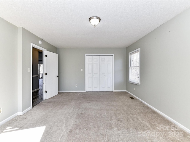 unfurnished bedroom featuring carpet, a closet, a textured ceiling, and baseboards