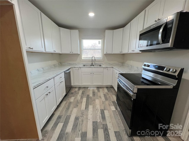 kitchen featuring stainless steel appliances, light stone counters, a sink, and light wood-style floors