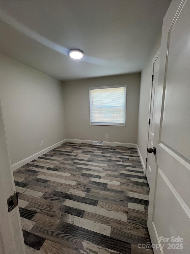 spare room featuring wood finished floors, visible vents, and baseboards