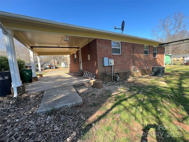 rear view of property featuring a yard, a carport, brick siding, and central AC unit