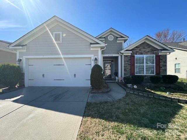 view of front of property with a front lawn, stone siding, driveway, and an attached garage