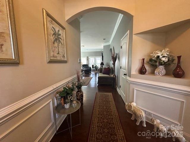 hall featuring arched walkways, a wainscoted wall, crown molding, and a decorative wall