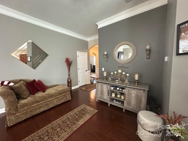 living room featuring arched walkways, baseboards, dark wood-style floors, and crown molding