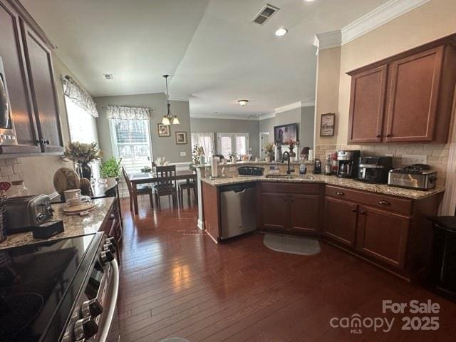 kitchen with light stone counters, stainless steel appliances, hanging light fixtures, a sink, and a peninsula