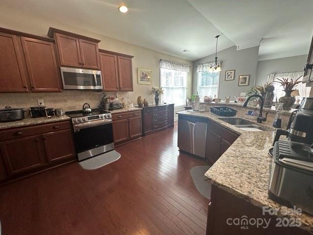 kitchen featuring stainless steel appliances, dark wood-style flooring, a sink, light stone countertops, and decorative light fixtures