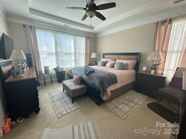 carpeted bedroom featuring a tray ceiling, a ceiling fan, visible vents, and crown molding