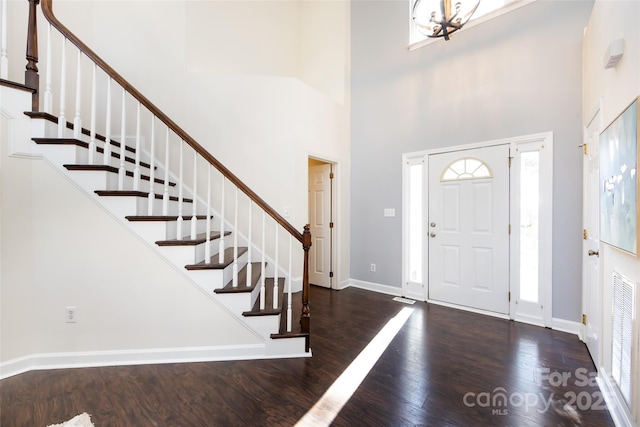 foyer entrance with dark wood-style floors, a chandelier, a towering ceiling, and baseboards