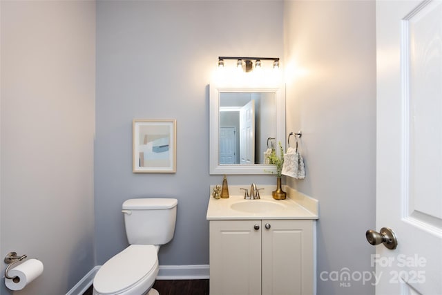 half bathroom featuring toilet, baseboards, and vanity